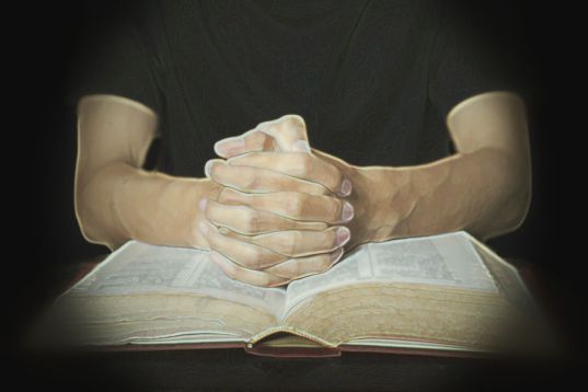 Closeup of hands in praying position with a bible
